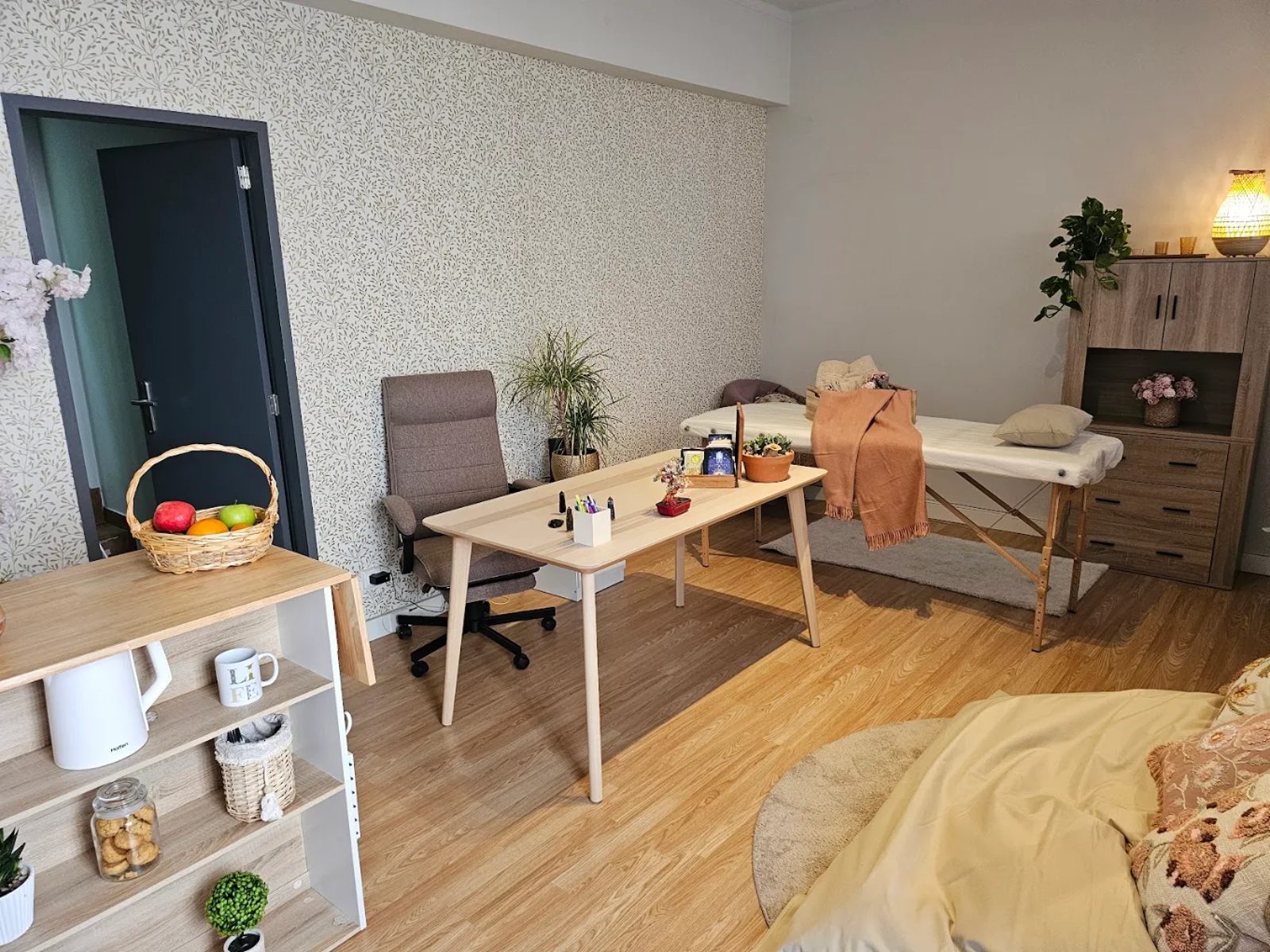 Vista da entrada: a porta escura ao lado, e a sala se abrindo com a mesa de trabalho e a maca ao fundo